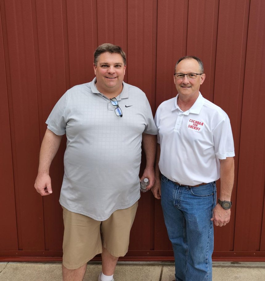 Two men standing next to each other in front of a red wall.